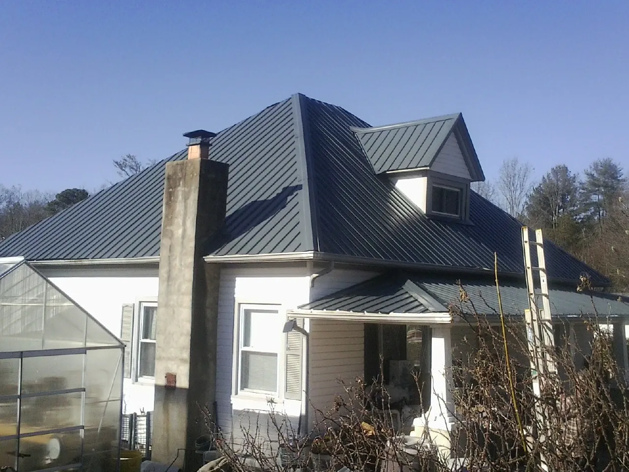 Dark blue standing seam metal roof on a white farmhouse with dormer — Slate & Tile Roof Repair by Roofing Brothers in Fruitvale