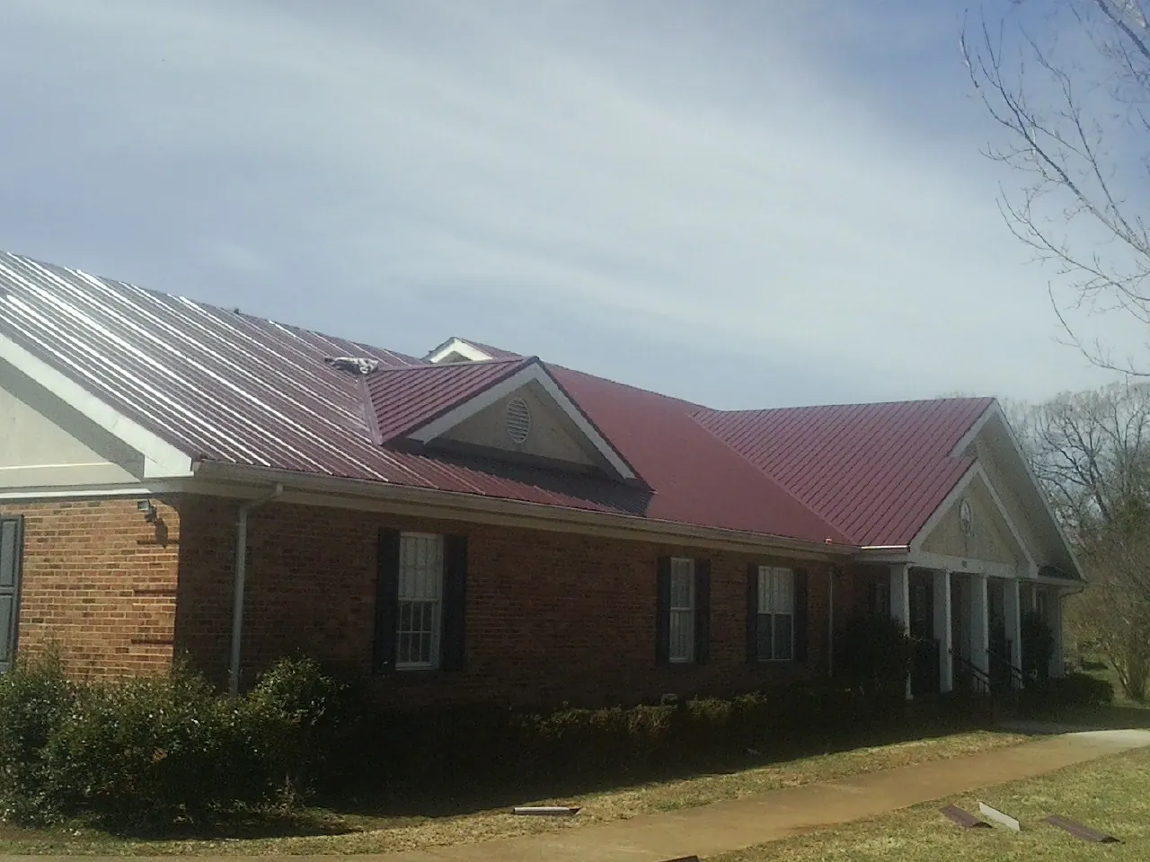 Red metal roof with gabled entries on a long brick building, from a Hail Damage Roof Repair job in Fruitvale
