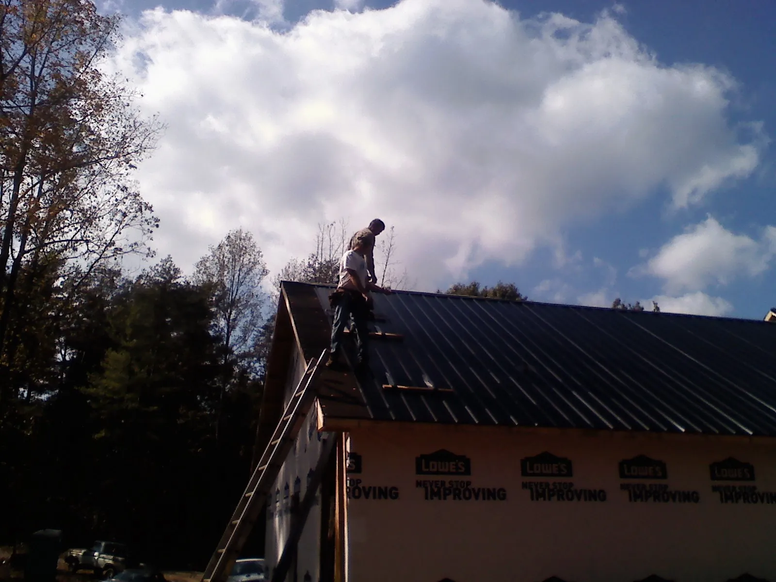 Roofer fastening dark metal panels high against a cloudy sky, from a Roof Inspection job in Fruitvale